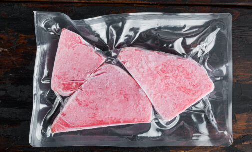 Frozen tuna steak vacuum pack, on old dark wooden table background, top view flat lay