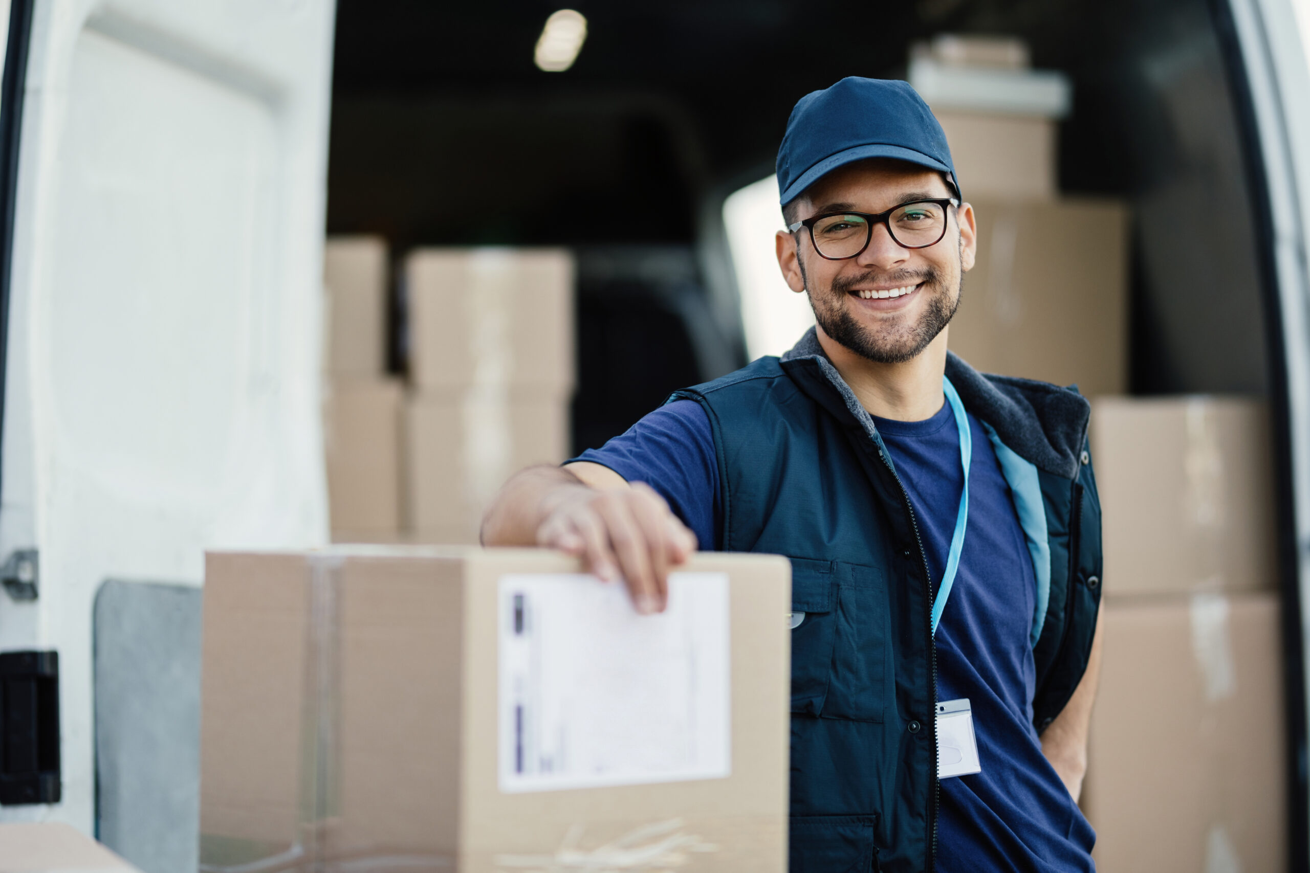 Young happy delivery man with cardboard boxes looking at camera.